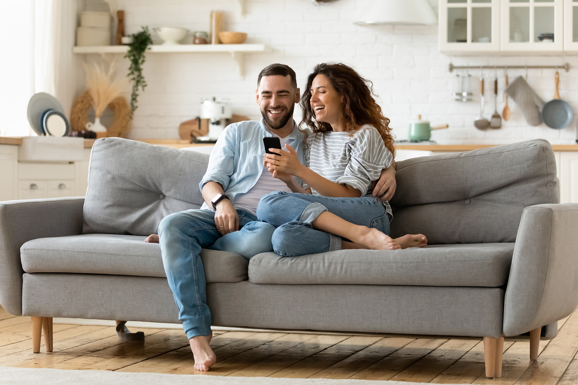 A couple on a couch laughing while looking at a cell phone.