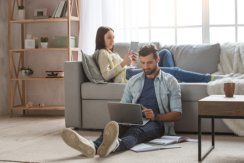 Couple in living room on devices and relaxing.