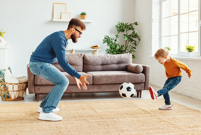 Father and toddler son playing soccer in the living room.