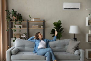 Smiling woman using air conditioner remote controller, switching temperature