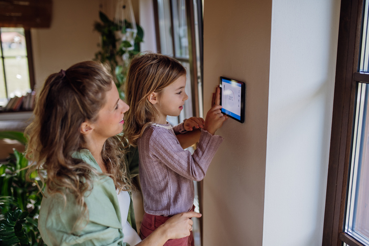 Girl helping mother to adjust thermostat.