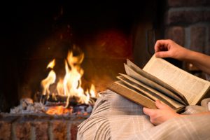 Person reading a book by a fireplace