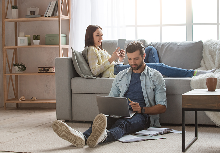 Couple in living room on devices and relaxing.