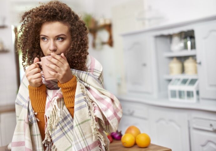 Young woman wrapped in blanket drinking hot tea