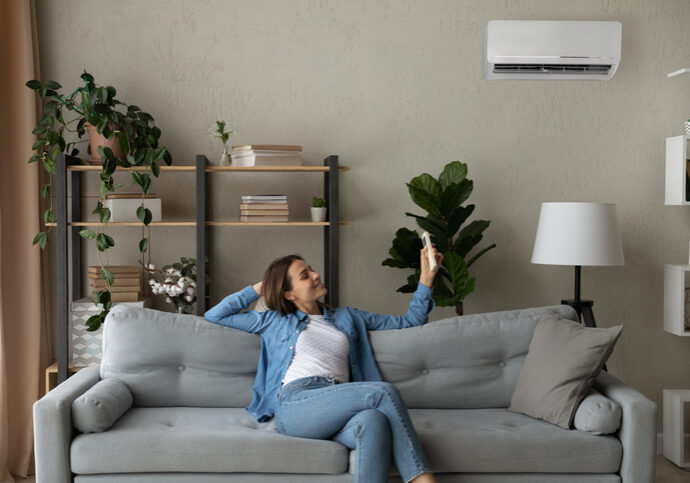 Smiling woman using air conditioner remote controller, switching temperature