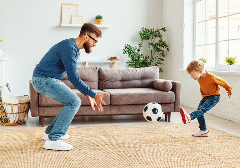 Father and toddler son playing soccer in the living room.