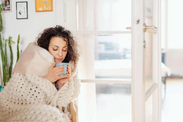 A woman wrapped in a blanket holding a blue mug.